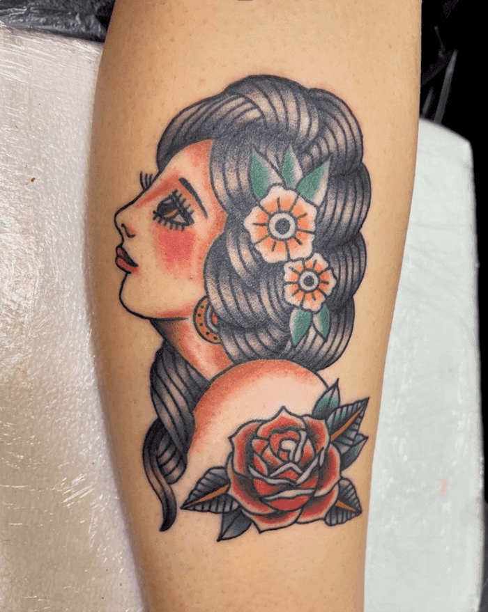 American traditional tattoo of a woman in profile with flowers in her hair and a rose, in bold outlines with red and green