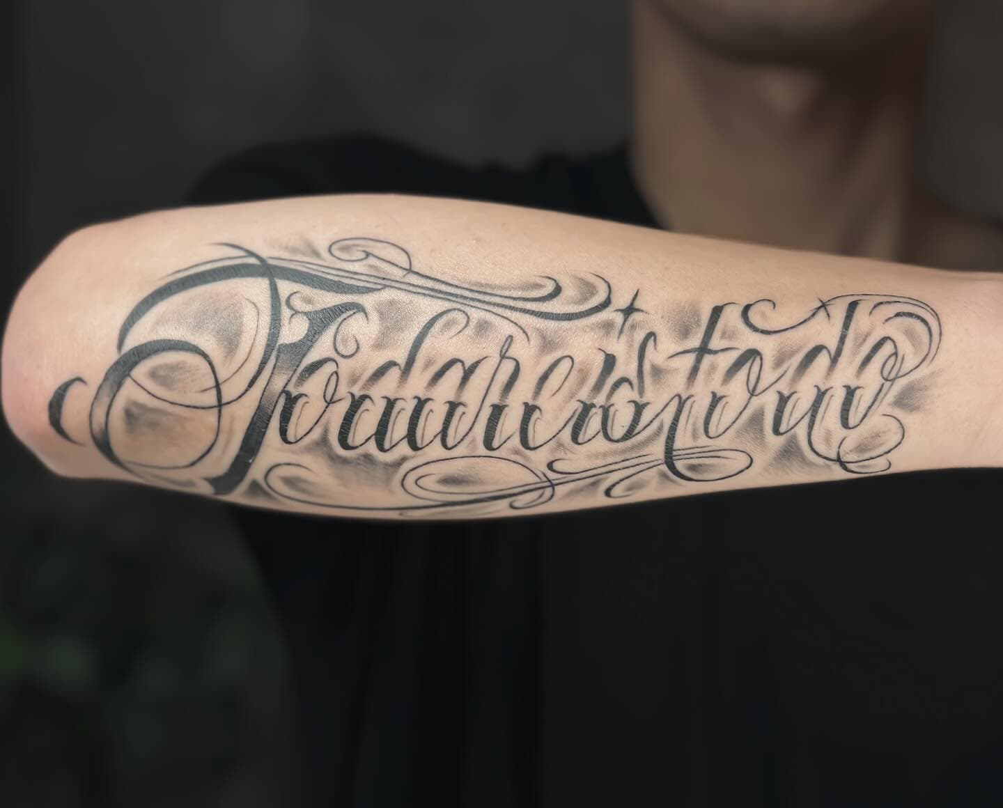 Black and grey forearm tattoo of cursive script with soft gray shading